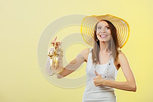 Woman in big yellow summer hat holds sandals