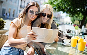 Holidays, tourism and internet - beautiful girls looking at tablet pc in cafe outside