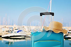 Holidays. travel concept. blue suitcase with female hat, sunglasses in front of tropical marina background