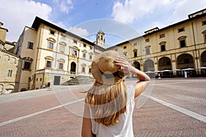 Holidays in Tuscany. Rear view of traveler girl holds hat in Piazza Grande square in the old town of Arezzo, Tuscany, Italy photo