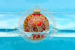 Holidays and vacation concept. Festive decoration for Christmas tree, red ball with glitter decor dropped into water