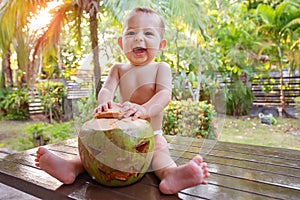 Holidays vacation concept. Little child infant shouts while sitting on the table. It holds coconut which is made as a symbol of