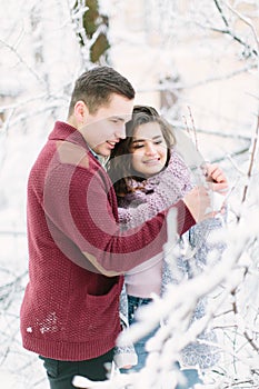 Holidays, winter, christmas, hot drinks and people concept - happy couple in warm clothes hugging near the tree branches