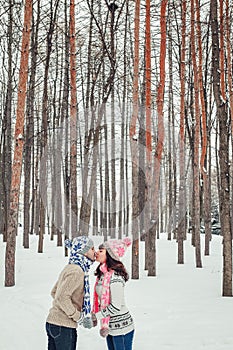 Holidays, winter, christmas, love and people concept - happy couple kissing in forest among fir trees in snow