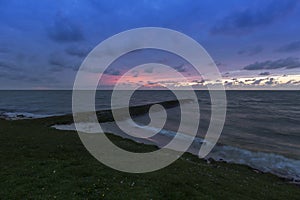 Holland - Sunset over the stormy sea. A stone rampart jutting out into the sea. in the foreground sand and green grass