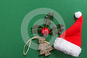 Holly berry made from fresh leaves bright red Christmas ornament ball wooden tree Santa Claus hat on dark green background