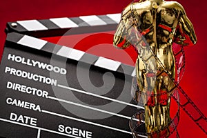 Hollywood film awards concept with shiny metallic movie award wrapped in celluloid film strip on red carpet with clapper board