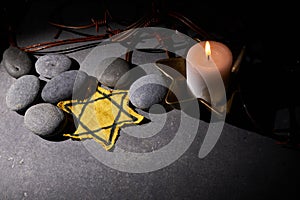 Holocaust memory day. Barbed wire, stones, yellow star and burning candle on black background