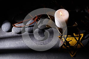 Holocaust memory day. Barbed wire, stones, yellow star and burning candle on black background