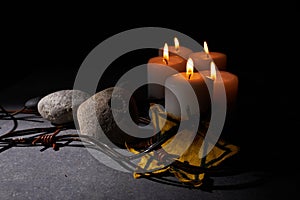 Holocaust memory day. Barbed wire, stones, yellow star and burning candle on black background