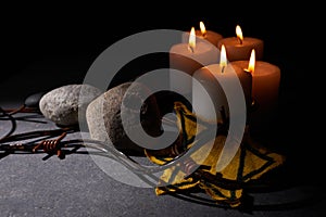 Holocaust memory day. Barbed wire, stones, yellow star and burning candle on black background