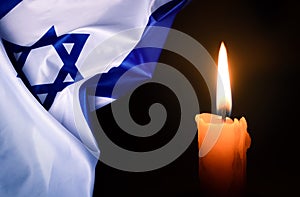 Holocaust Remembrance Day. Yom HaShoah. Bright Burning Candle and the official flag of Israel on a dark grey background.