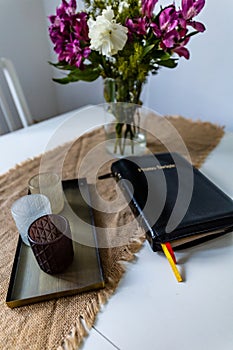 Holy Bible with black cover lie on wooden table next to flowers and candles