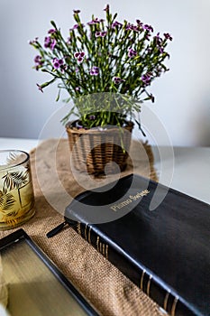 Holy Bible with black cover lie on wooden table next to flowers and candles