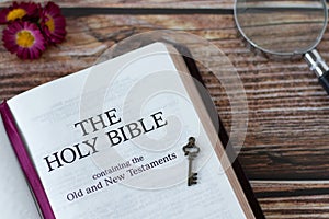 Holy Bible Book with ancient key and magnifying glass on wooden background, top view.