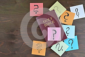 Holy bible and colorful note pads with question marks on brown wood