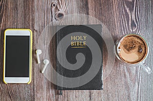 The Holy Bible with headphones, a phone and a hot cup of coffee. Reading the bible.