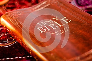 Holy Bible King James Version with pressed decorative leather cover on table with soft flickering candlelight