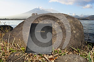 Holy Bible leaning against a rock on the shore of Lake Kawaguchi with the majestic Mount Fuji in the background, Japan