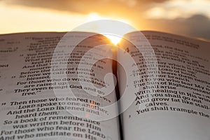 Holy Bible open at sunset with highlight on Malachi 4:2. Background with clouds and sun