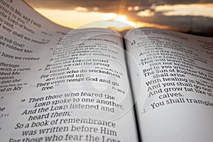 Holy Bible open at sunset with highlight on Malachi chapter 4 verse 2. Background with sun and clouds