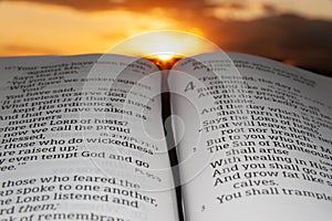 Holy Bible opened at sunset, highlighted in Malachi chapter 4 verse 2. Background with sun rays and clouds