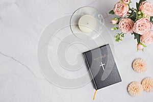 Holy Bible with pink roses and candle over the light marble background.