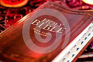 Holy Bible with pressed decorative leather cover on table with soft flickering candlelight