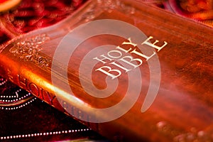 Holy Bible with pressed decorative leather cover on table with soft flickering candlelight