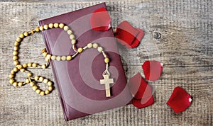 Holy Bible, rosary and red rose petals