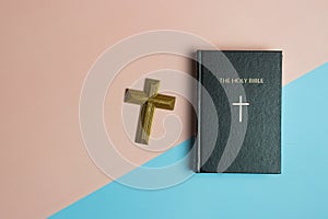 Holy Bible with a wooden cross on pink and blue background.