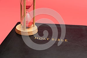 Holy Bible, the Word of God with hourglass. Isolated on red background. Top view. Close-up. Copy space. Horizontal shot