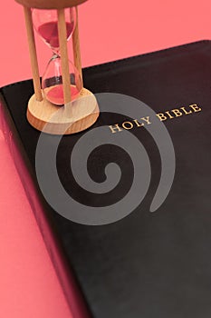 Holy Bible, the Word of God with hourglass. Isolated on red background. Top view. Vertical shot