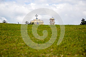 Holy cathedral church through the green hilly mountain. The Christian church, cross, and statue of jesus christ against cloudy sky