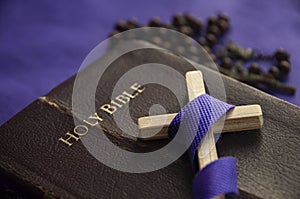 Holy cross on Bible with Rosary and purple cover background. Religious concept