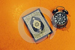 Holy Quran with Arabic calligraphy meaning of Al Quran, alarm showing 7 o` Clock