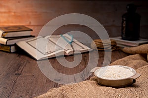 Holy Quran and a grain of rice in a wooden bowl in the sack on a wooden table, Islamic zakat concept.