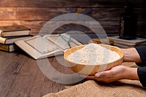 Holy Quran and a grain of rice in a wooden bowl in the sack on a wooden table, Islamic zakat concept.