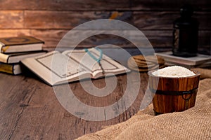 Holy Quran and a grain of rice in a wooden bowl in the sack on a wooden table, Islamic zakat concept.