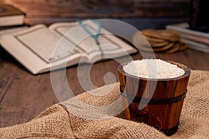 Holy Quran and a grain of rice in a wooden bowl in the sack on a wooden table, Islamic zakat concept.