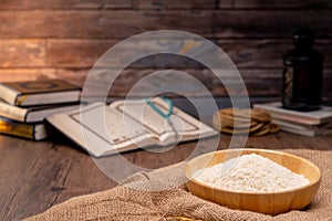 Holy Quran and a grain of rice in a wooden bowl in the sack on a wooden table, Islamic zakat concept.