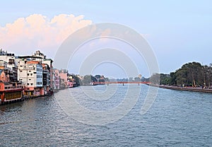 The Holy River Ganges - Ganga with both Banks, Buildings and White Clouds in Blue Sky - Haridwar, Uttarakhand, India