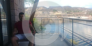 Hombre latino con vista de lago y montaÃÂ±a desde la terraza con mesa y sillas de madera al amanecer photo