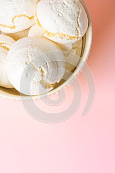 Home baked meringue cookies in white bowl on light pink background. French Italian Swiss cuisine confection coffee dessert