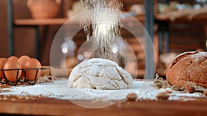 Home bakery, raw dough on wooden kitchen table with fresh bread and eggs, flour pouring from up