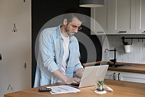 Confident young male provide payments online using laptop at kitchen photo
