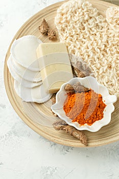 Home beauty products - turmeric, soap, scrub, sponges, soap, facial brush on light background, top view. Skin youthfulness, beauty