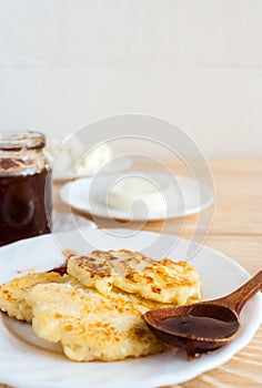 Curd pancakes, soft cheese, fresh curd and plum jam in jar and on wooden spoon on wooden table and copy space.