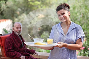 Home carer serving meal to elderly man