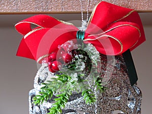 Home Christmas decoration. A silver ball. small green Christmas tree branch, red ribbon and mistletoe on light blurred background.